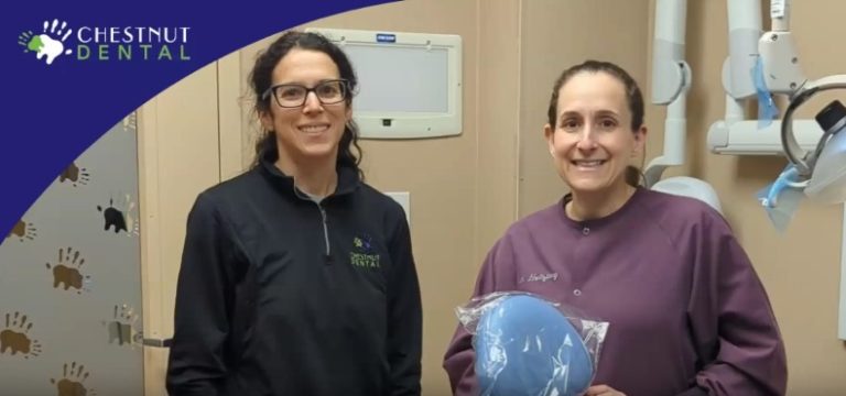 Two female dental professionals stand in a dental office; one wears a black jacket, the other holds a dentistry item and wears a purple coat. "Chestnut Dental" logo appears in the corner.