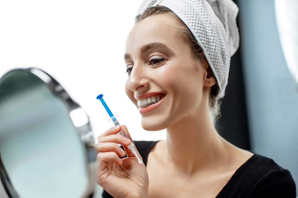 Woman looking at teeth holding syringe
